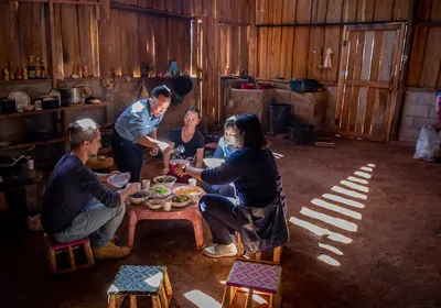 Matthieu Groussin sits with three other people on stools in front of a low table, on which there are several bowls of food. Another person stands above Groussin spooning something into a bowl.